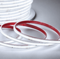 A coiled portion of high voltage COB LED light strip glowing with cool white light, shown in close-up against a warm beige background, next to the original spool of COB light strip.